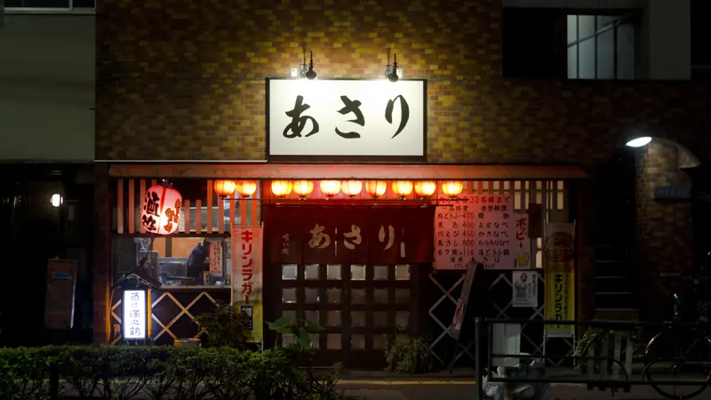 A small izakaya in Gotanda, Tokyo at night, with a row of glowing red lanterns under its hiragana sign