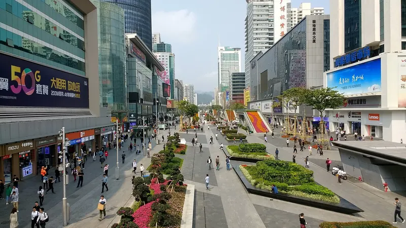 The Huaqiangbei pedestrian street in Shenzhen's electronics district, lined with shops, screens and flower beds on a sunny day