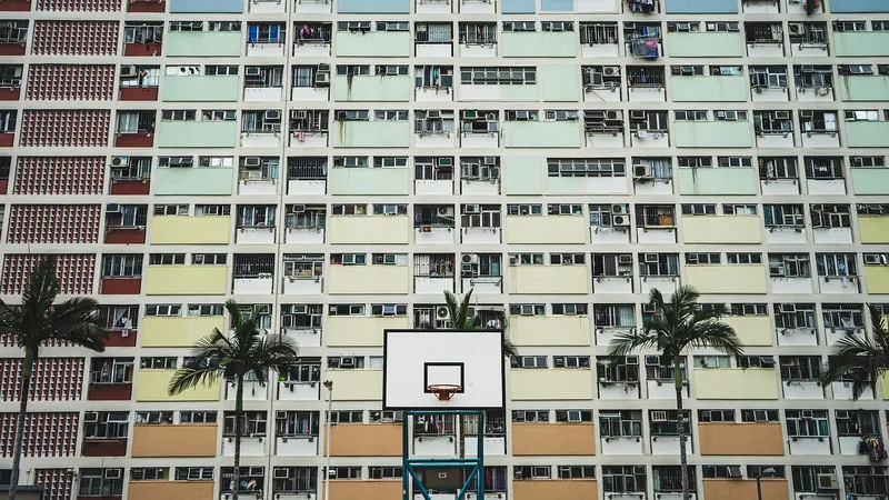 Pastel-coloured apartment blocks of Choi Hung Estate in Hong Kong behind a basketball hoop and palm trees