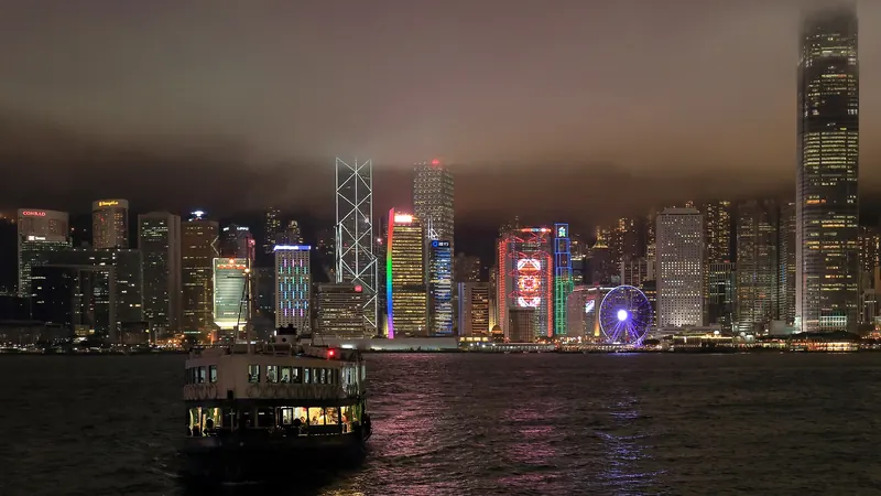 A Star Ferry crossing Victoria Harbour at night, with the lit Hong Kong Island skyline under low cloud behind it