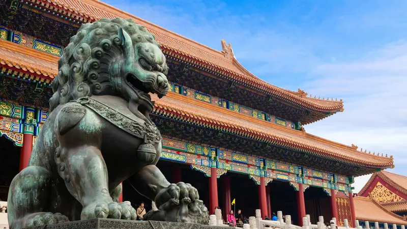 A bronze guardian lion statue in front of the Hall of Supreme Harmony in the Forbidden City, Beijing, under a blue sky