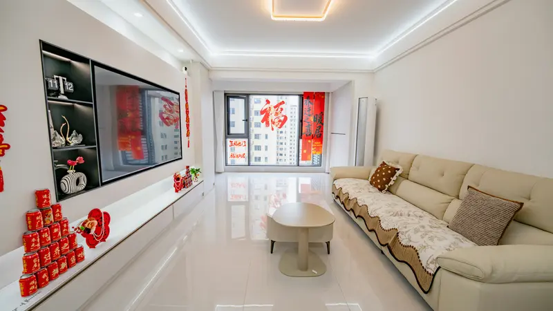 A bright apartment living room with a cream sofa, a wall-mounted TV and red Lunar New Year decorations on the window
