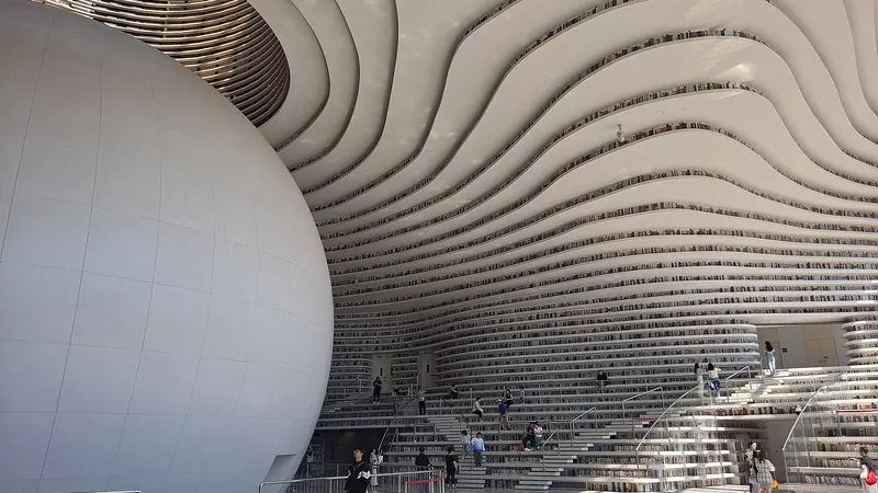 The atrium of Tianjin Binhai Library, with wave-shaped white terraces of bookshelves curving around a large white sphere