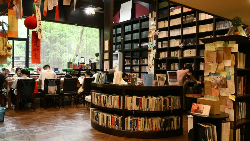 People reading at tables in a bookstore cafe in Hangzhou with curved bookshelves and red lanterns