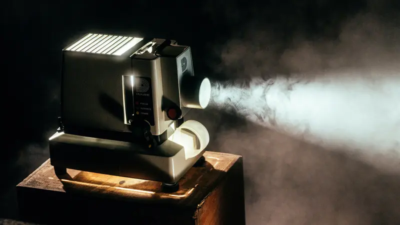 A small film projector on a wooden box casting a beam of light through haze in a dark room