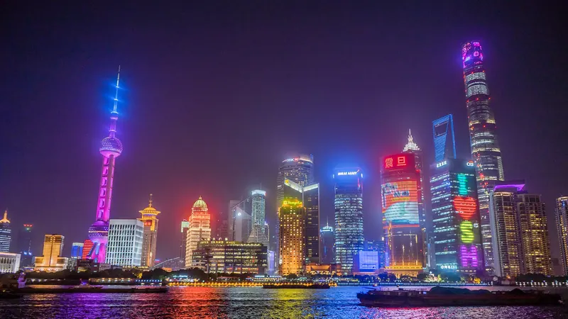 The Lujiazui skyline in Shanghai at night, with the Oriental Pearl Tower and skyscrapers lit in neon colours over the Huangpu River