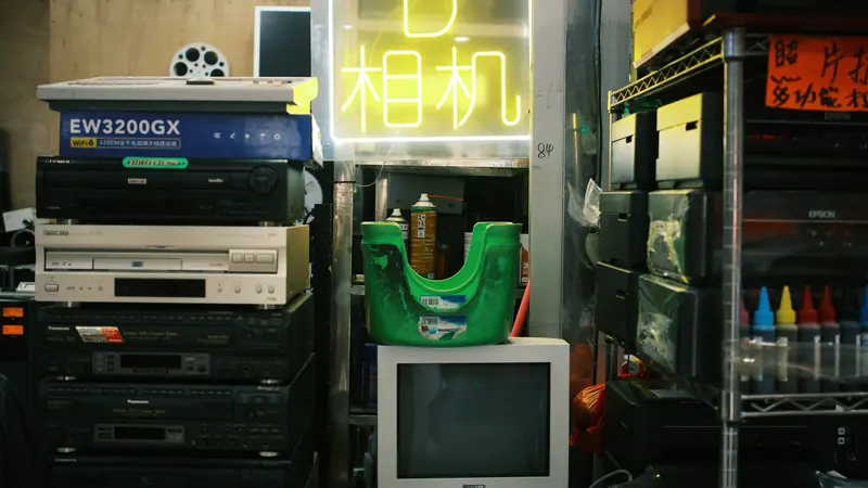 Small electronics shop in Guangzhou with stacked video players, an old television and a yellow neon sign in Chinese