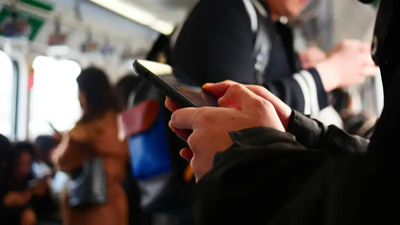 Close-up of hands holding a smartphone on a crowded Beijing subway car, other passengers blurred behind