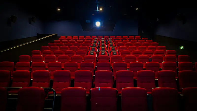 Empty cinema with rows of red seats and a projector light at the back of the dark room