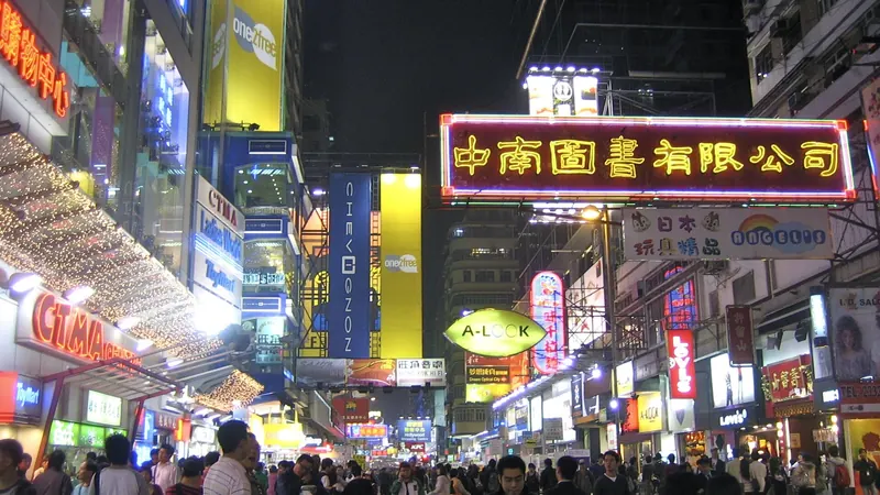 A crowded shopping street in Hong Kong at night under glowing neon signs in Chinese characters