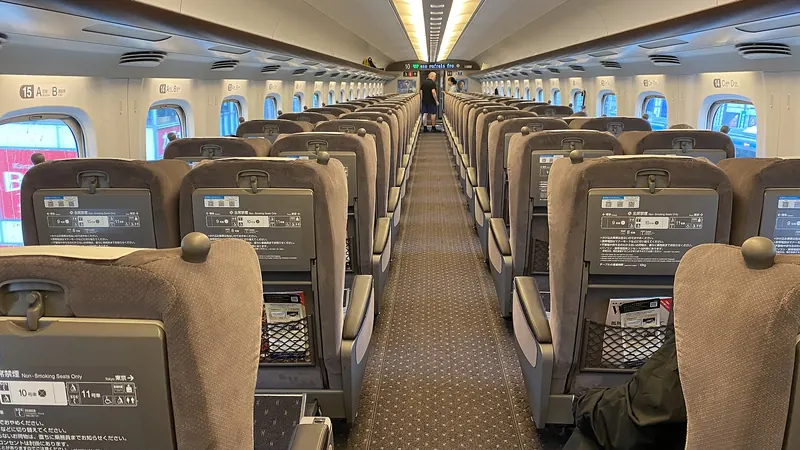 Rows of grey reclining seats along the aisle of a Shinkansen bullet train carriage
