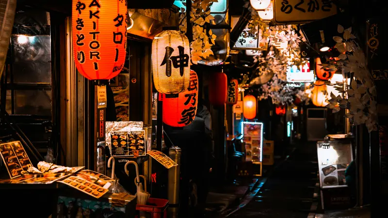 Red and white paper lanterns glowing over small food stalls in the narrow Omoide Yokocho alley in Shinjuku at night