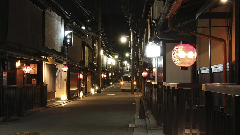 A quiet street in Kyoto's Gion district at night, lined with dark wooden townhouses and glowing paper lanterns