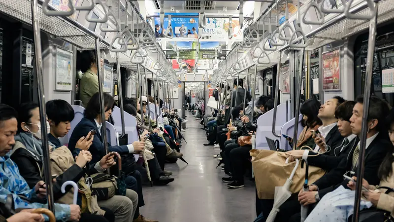 Passengers seated along both sides of a Tokyo subway car, many looking at their phones
