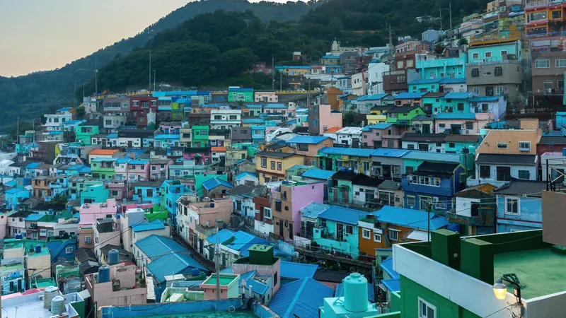 Colorful hillside houses of Gamcheon Culture Village in Busan, South Korea, at sunset below a green mountain