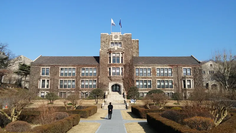 A stone university hall with a central tower on the Yonsei University campus in Seoul, under a clear blue sky
