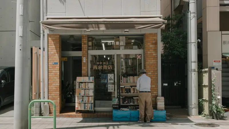 A man browsing the outdoor shelves of a small secondhand bookstore on a Tokyo street