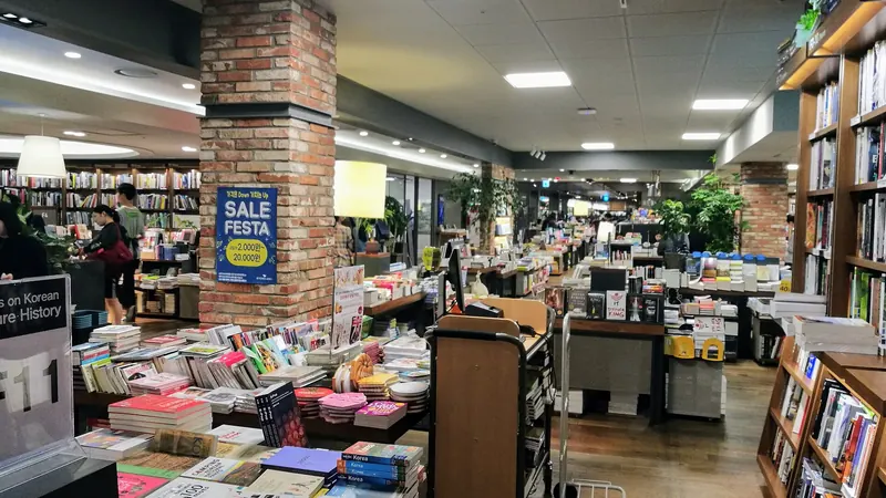 Shoppers browsing long tables and shelves of books inside a Kyobo bookstore in Seoul, under bright ceiling lights