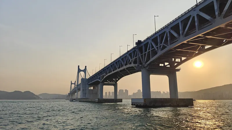Gwangan Bridge stretching across the water at Gwangalli in Busan, with the sun setting through a warm haze