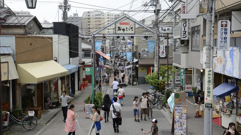 People strolling down the small shopping street of Yanaka Ginza in Tokyo, past its gateway sign and low shops