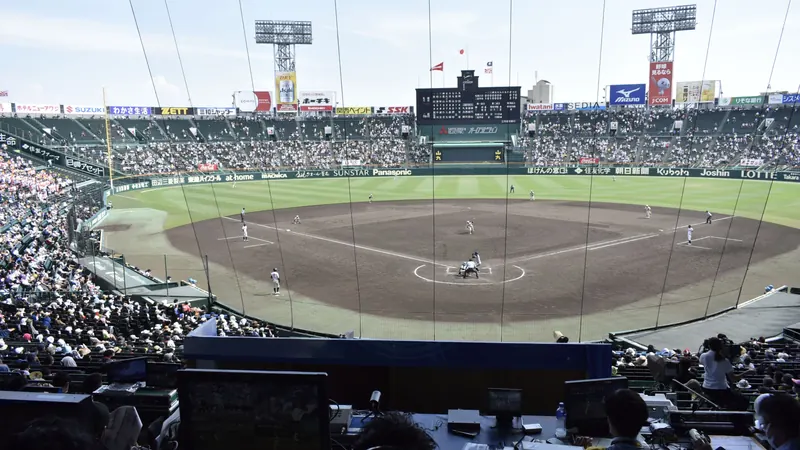 A high school baseball game at Hanshin Koshien Stadium, seen from high in the stands with crowds and the scoreboard