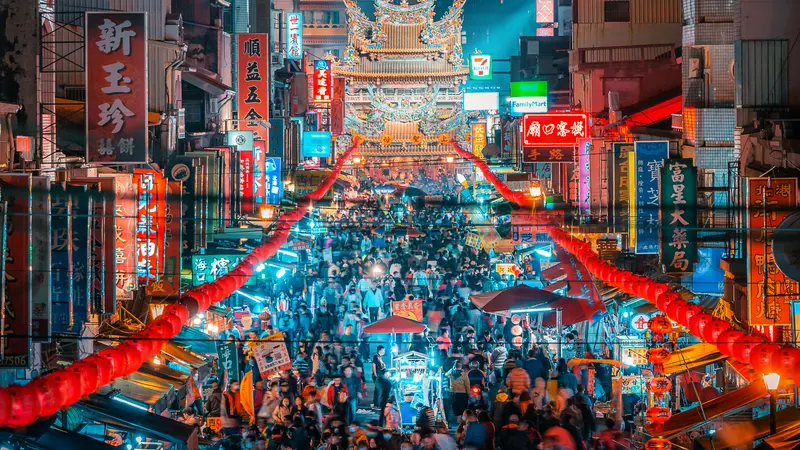 Calle abarrotada de un mercado nocturno en Taiwán, con farolillos rojos y letreros en caracteres chinos tradicionales y un templo ornamentado al fondo