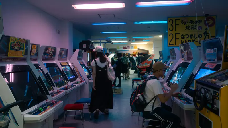 Rows of arcade cabinets in a Japanese game center, with a few people playing and a floor sign in Japanese