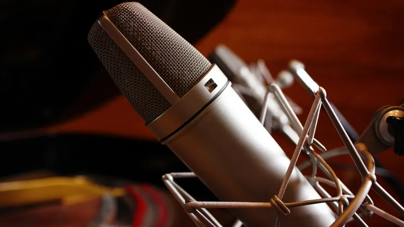 Close-up of a silver studio condenser microphone in a shock mount, lit warmly against a dark background