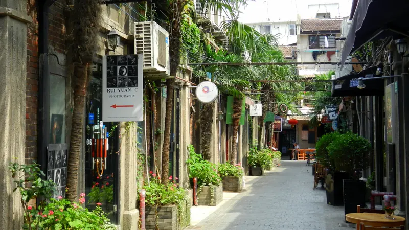 A narrow lane in Tianzifang, Shanghai, lined with old brick buildings, potted plants, palms and small shop signs