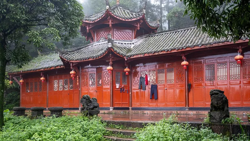 A red wooden Taoist temple hall with upturned eaves among misty forest trees on Mount Qingcheng, Sichuan