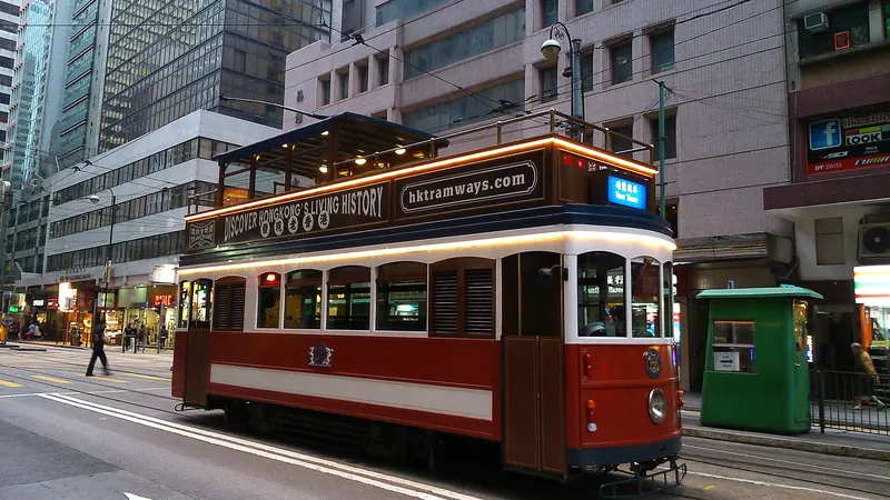 A red and cream heritage tram on a street in Sheung Wan, Hong Kong, between office towers and older buildings