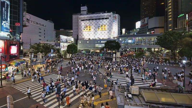 Crowds crossing the Shibuya scramble crossing in Tokyo at night, surrounded by lit buildings and screens