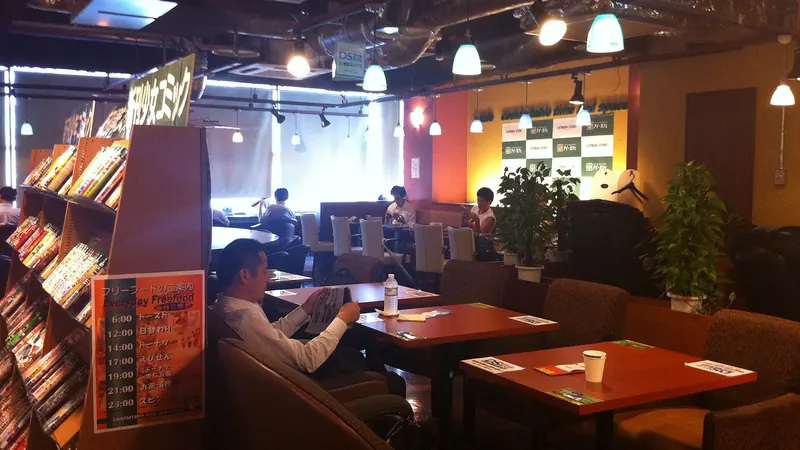 Inside a Tokyo manga cafe, with shelves of manga volumes beside booths and a reader at a table