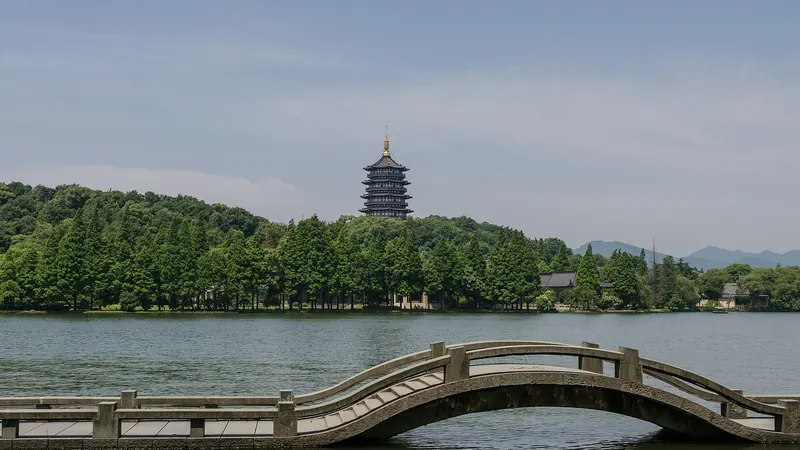 A low arched stone bridge on West Lake in Hangzhou, with Leifeng Pagoda rising above the wooded far shore