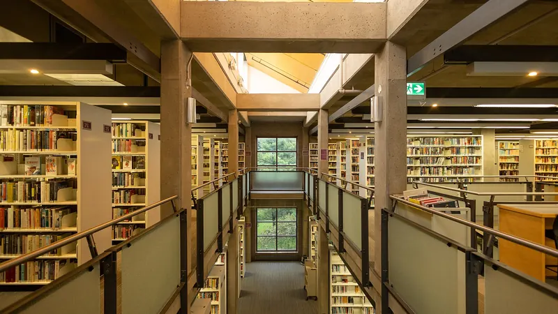 Rows of bookshelves on two levels of a public library, seen down a central walkway with railings