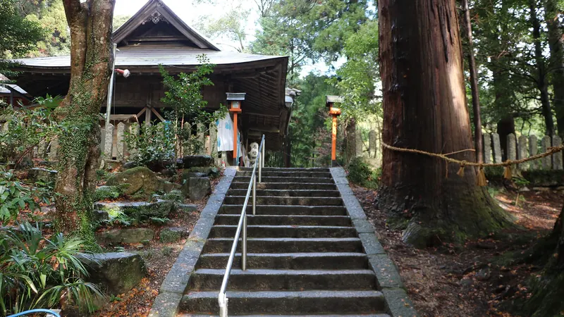 Stone steps with a metal handrail climbing through cedar trees to the wooden hall of Takakura Shrine in Iga, Mie