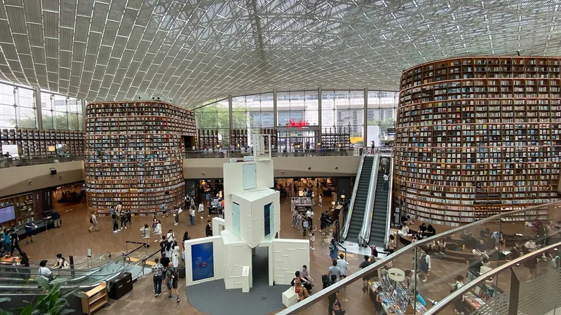Towering curved bookshelves under a glass lattice roof in the Starfield Library, a public library inside a Seoul mall