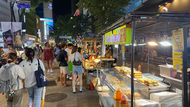 Street food stalls and strolling crowds on a busy Myeongdong shopping street in Seoul at night