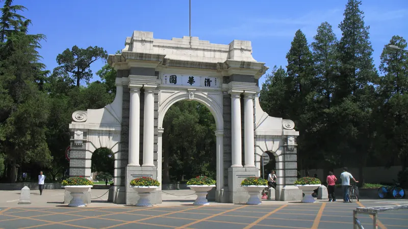 The white neoclassical Second Gate of Tsinghua University in Beijing, framed by tall trees under a blue sky