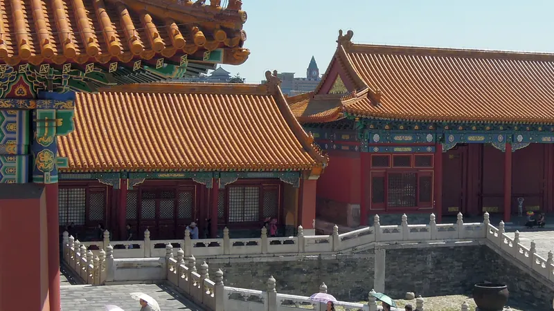 Red halls with yellow glazed roofs around a stone courtyard in the Forbidden City, Beijing, with visitors carrying parasols