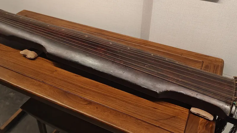 A Ming dynasty seven-string guqin zither in dark lacquered wood resting on a wooden stand in a museum
