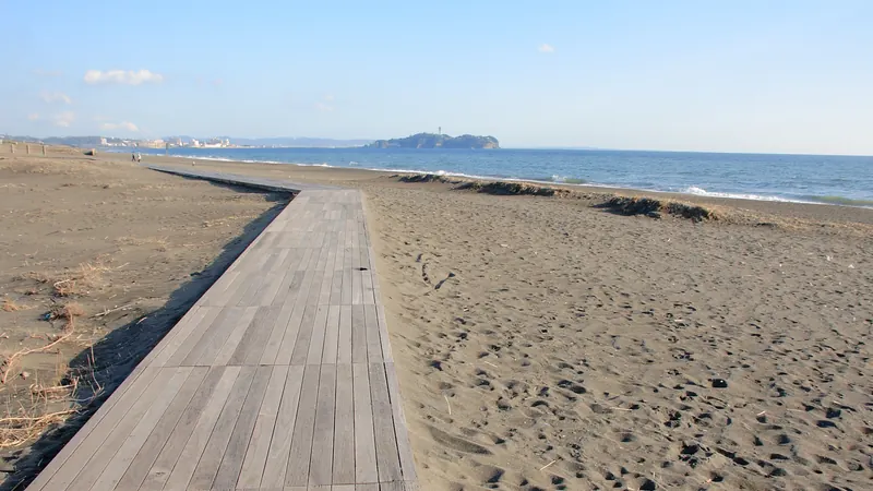 A wooden boardwalk across the sand of the Shonan coast toward the sea, with Enoshima island on the horizon