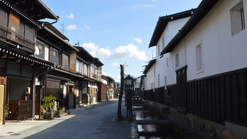 Traditional wooden houses and white storehouses beside the Seto River canal in Hida-Furukawa, Gifu, under a blue sky