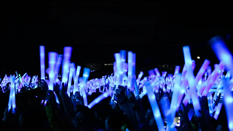 A concert crowd in the dark holding up glowing blue light sticks