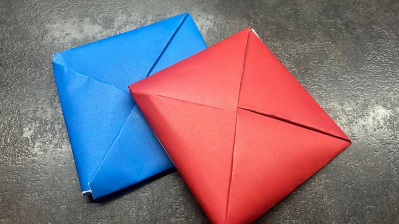 Two folded paper ddakji tiles, one blue and one red, lying on a dark stone surface