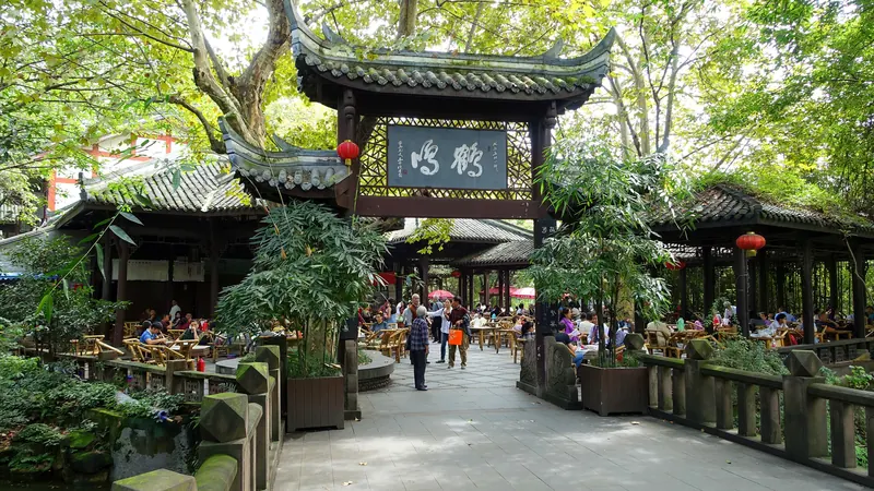 A busy open-air teahouse under trees in People's Park, Chengdu, with a carved gateway and red lanterns