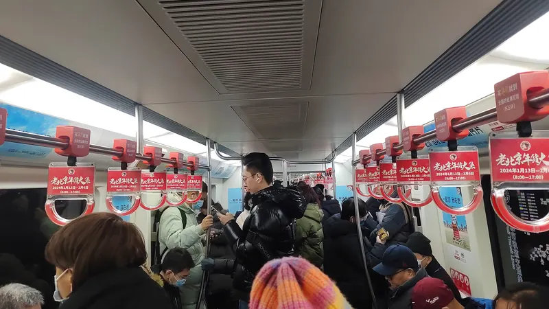 Commuters standing in a crowded Beijing Subway Line 10 carriage, several checking their phones under red hand straps